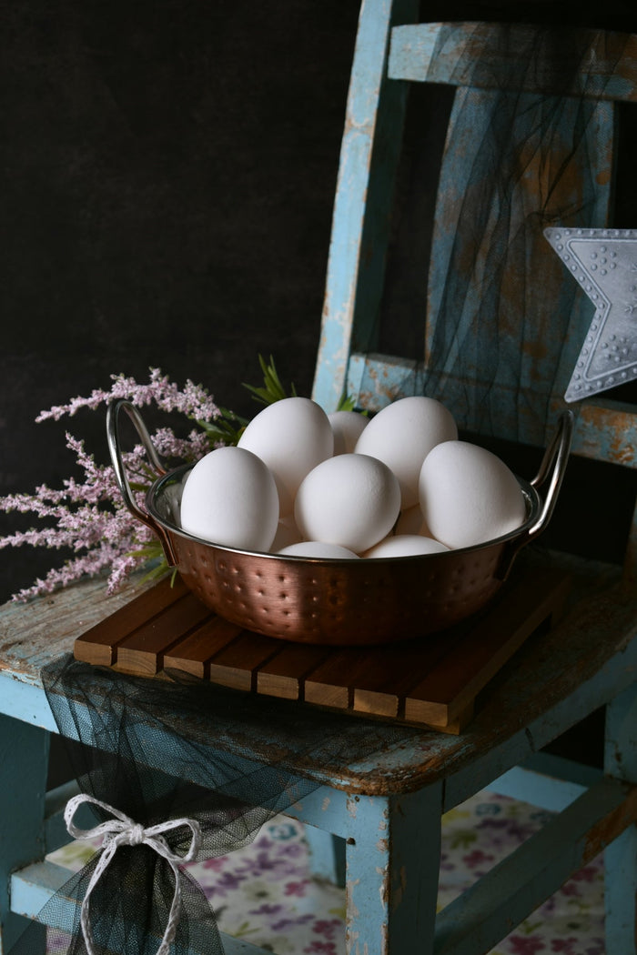 A metal bowl filled with white eggs sitting on top of a wooden table