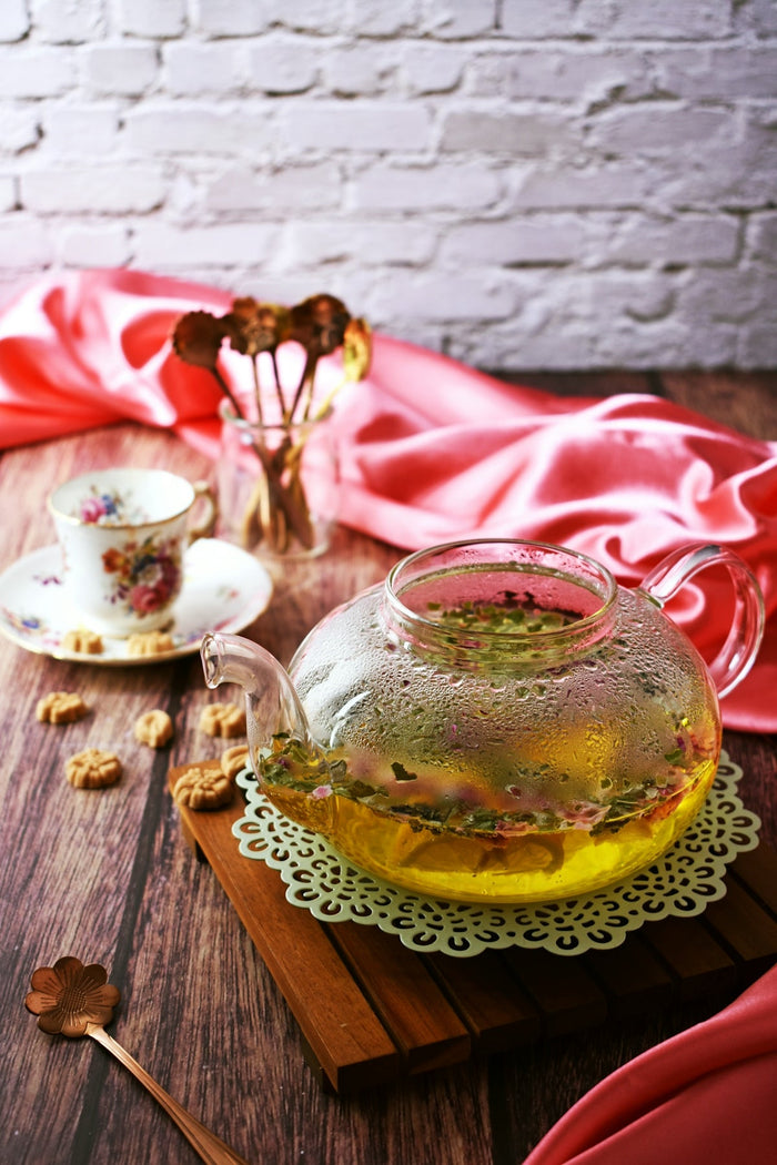 A glass tea pot filled with liquid sitting on top of a wooden table
